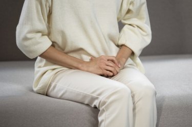 Ältere Frau mit Blasenentzündung sitzt am Bett und hält sich den Unterleib