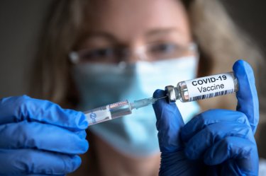 COVID-19-Impfstoff in den Händen der Forscher, weibliche Medizinerin hält Spritze und Flasche mit Impfstoff gegen Coronavirus.